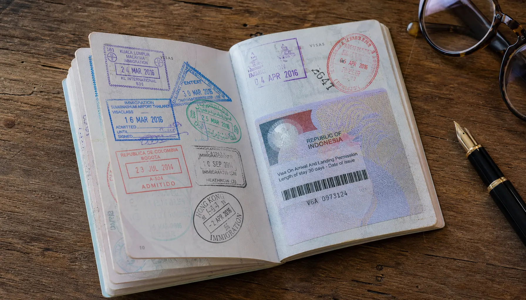 An open passport fanned across a desk, pages dense with colorful stamps beside a fountain pen.