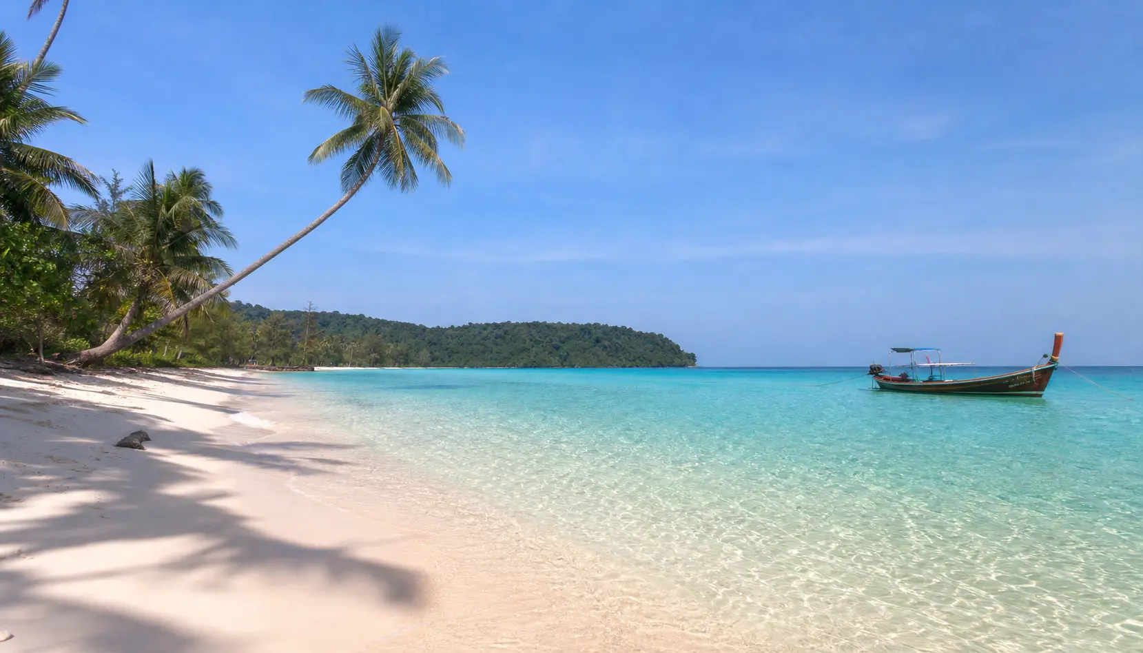 White-sand beach with palm trees, clear turquoise water and a longtail boat on Koh Rong, Cambodia