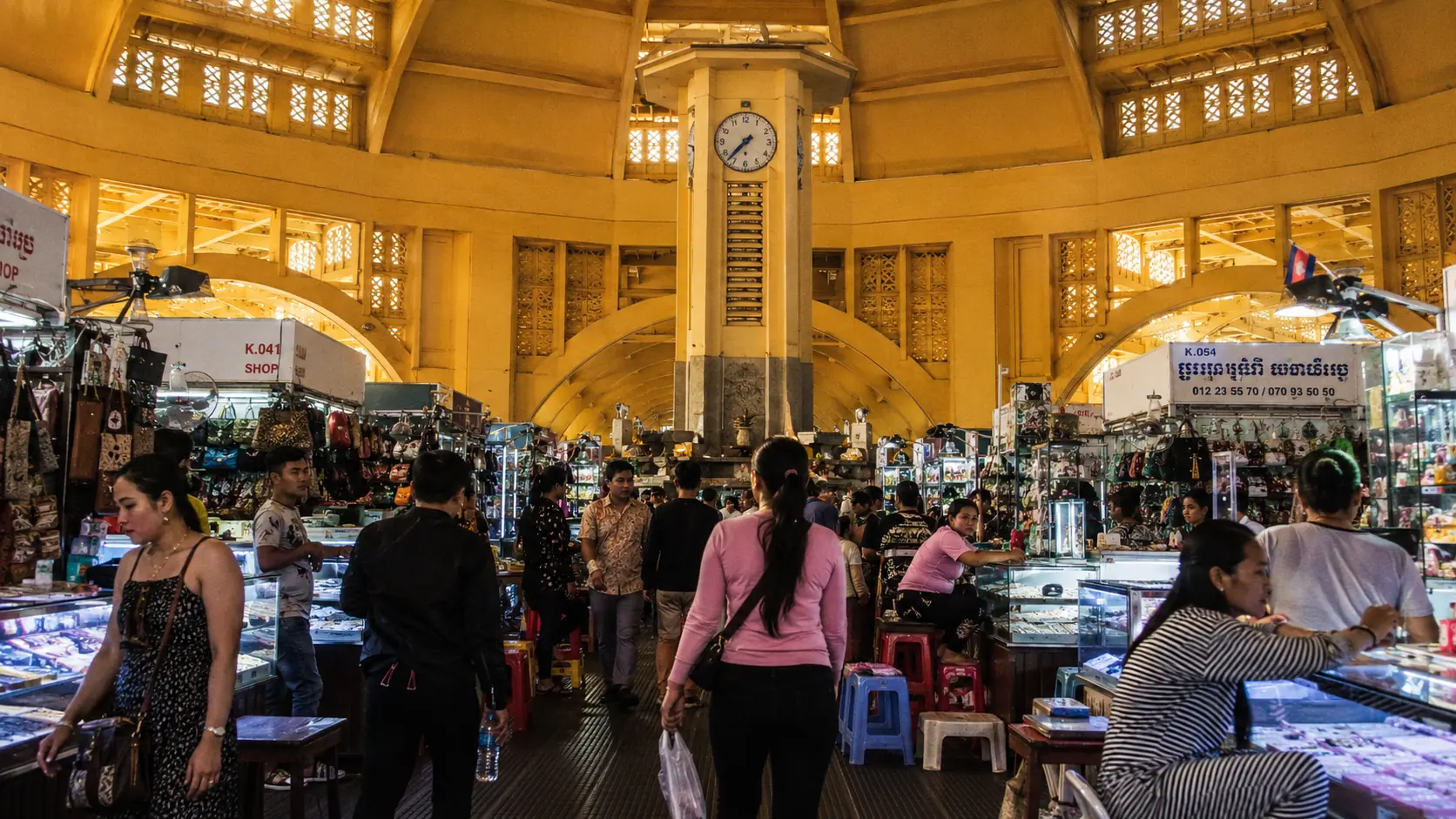 Narrow Siem Reap market alley lined with stalls of textiles, spices and souvenirs as shoppers browse under warm overhead lighting