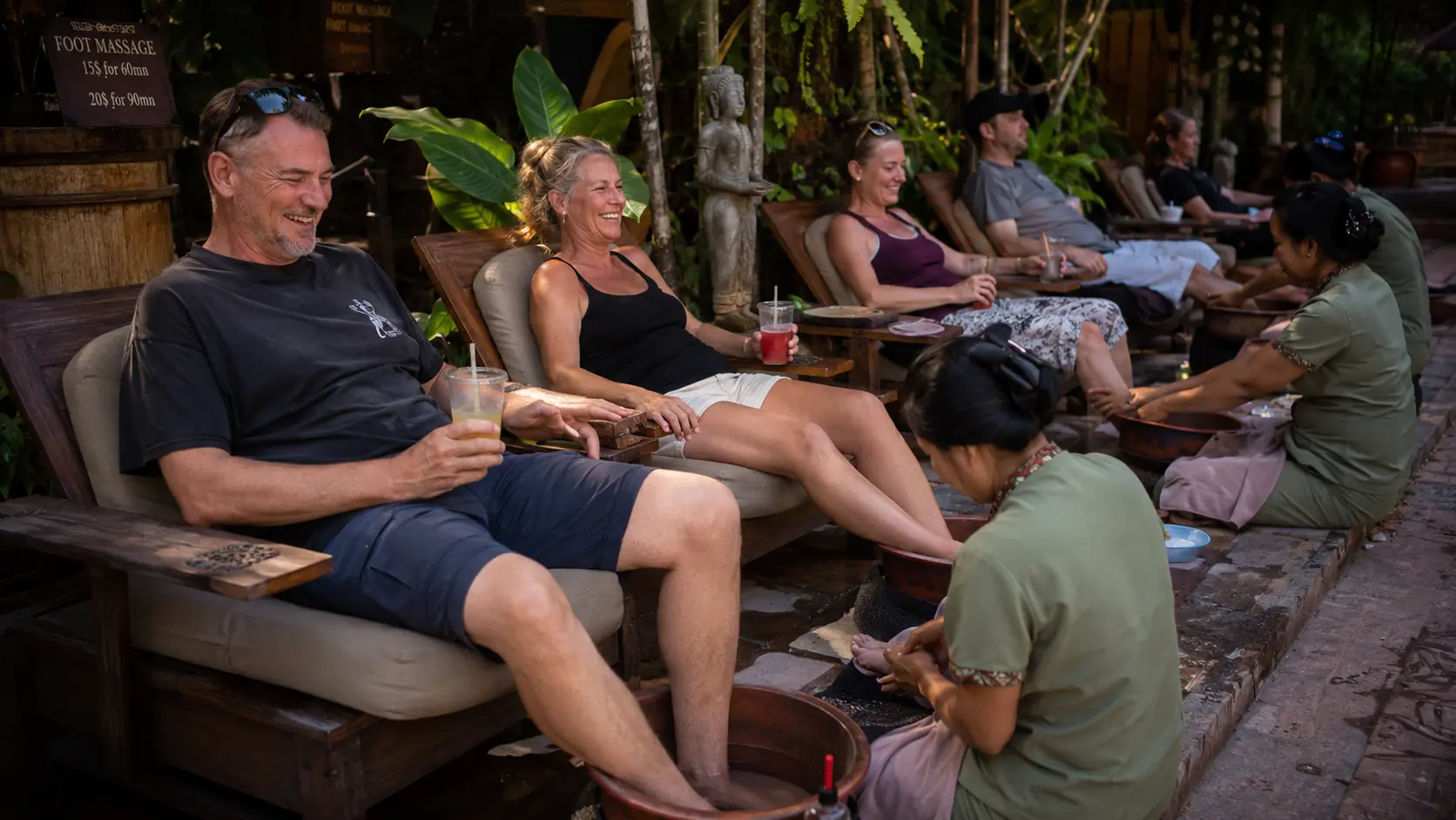 Tourists relaxing in reclining chairs while therapists give foot massages on a Pub Street side lane in Siem Reap, neon signs overhead