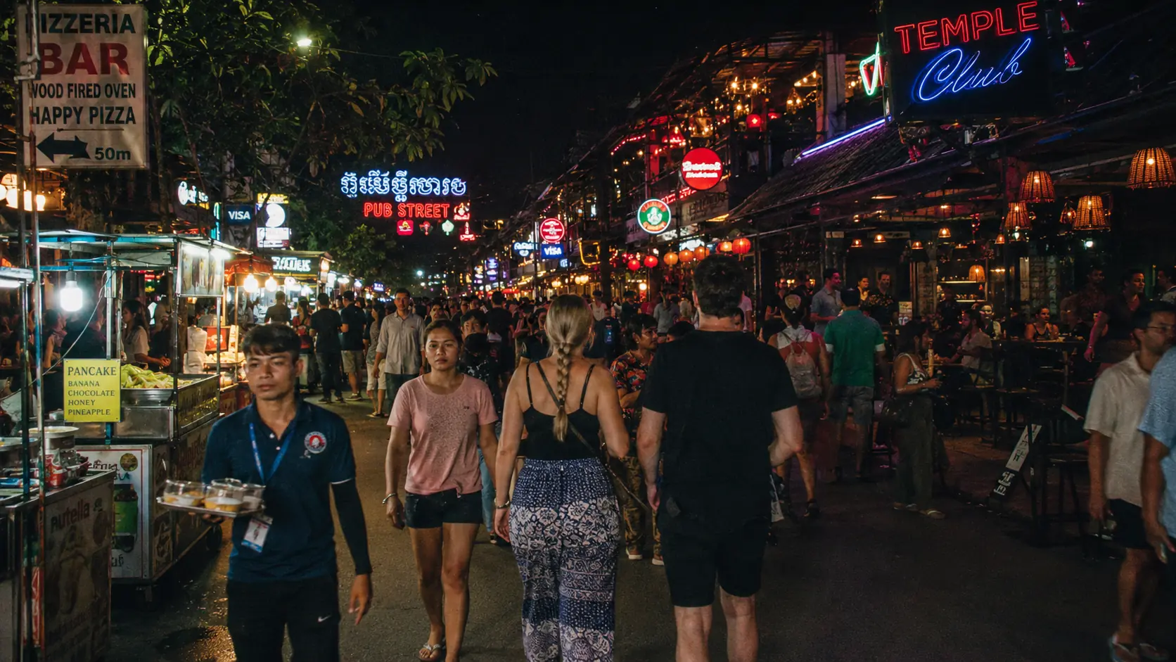 Vibrant Siem Reap walking street at night packed with crowds, glowing neon signs and tuk-tuks weaving between pedestrians