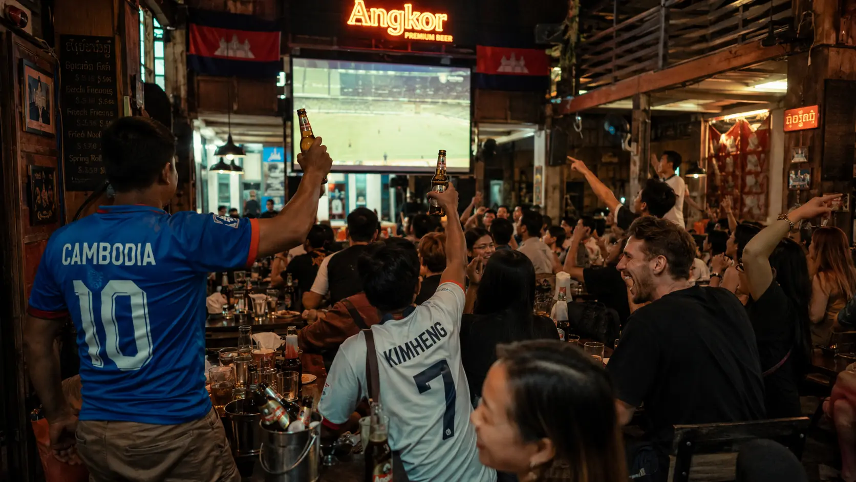 Sports bar in Phnom Penh with several flat-screens showing matches and patrons watching from high-top tables with Angkor Beer in hand