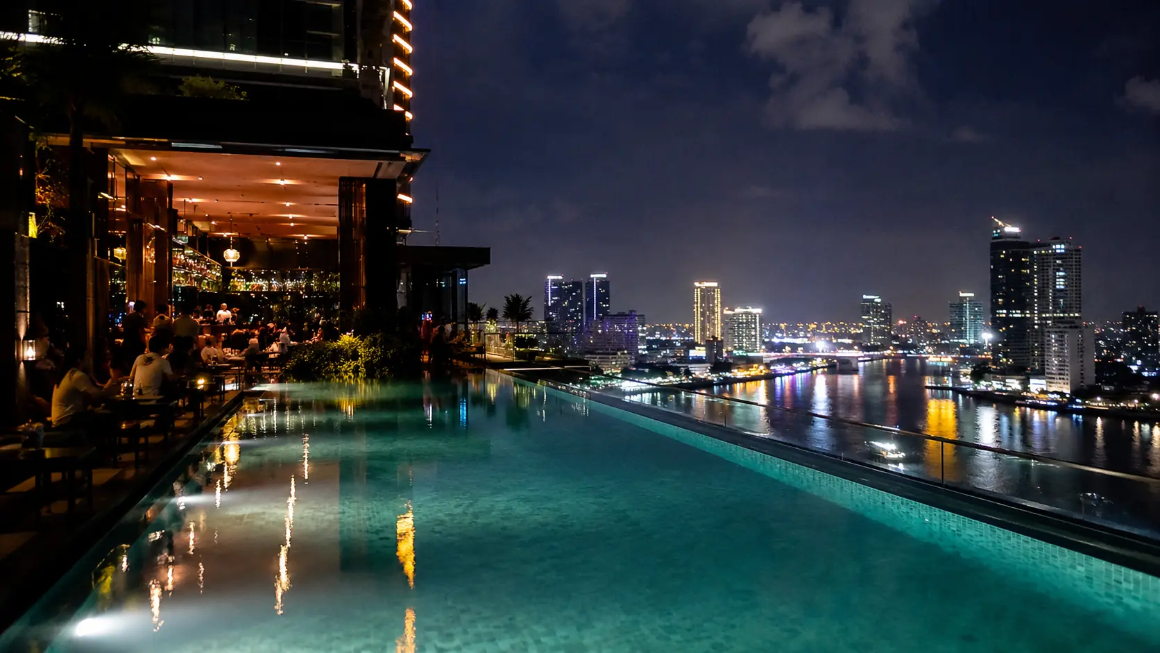 Phnom Penh sky bar with an infinity rooftop pool, skyline views beyond and patrons lounging on day-beds at golden hour