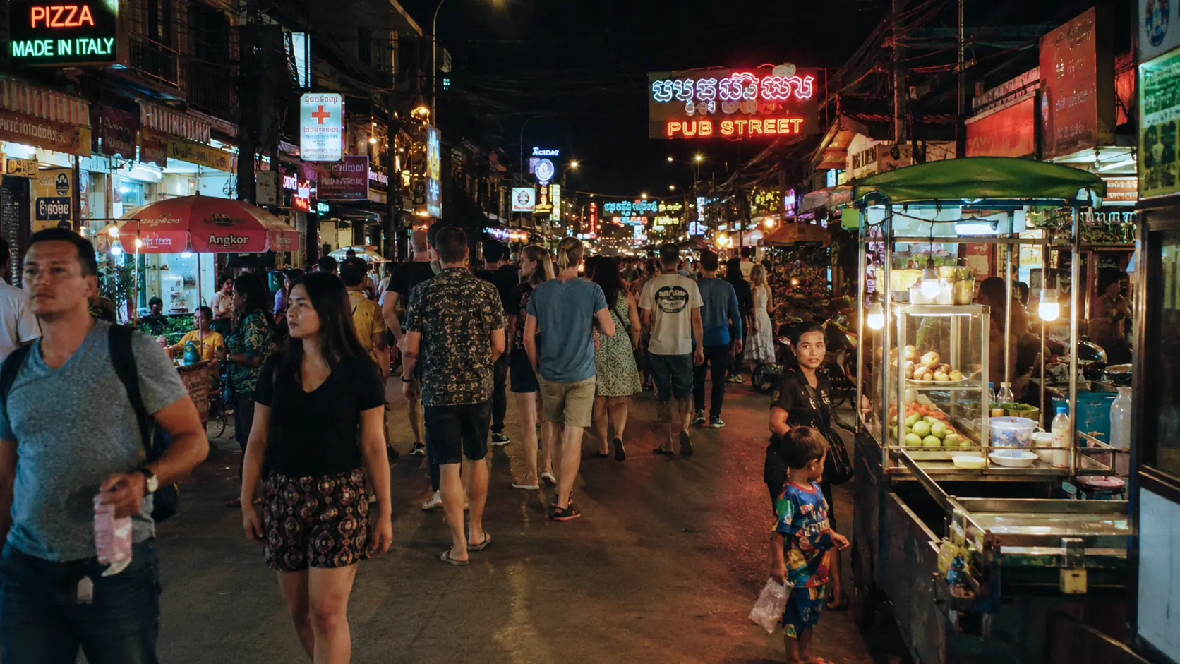 Brightly lit Siem Reap walking street with bar signs in English and Khmer, restaurant patios spilling onto the pavement and warm lantern light