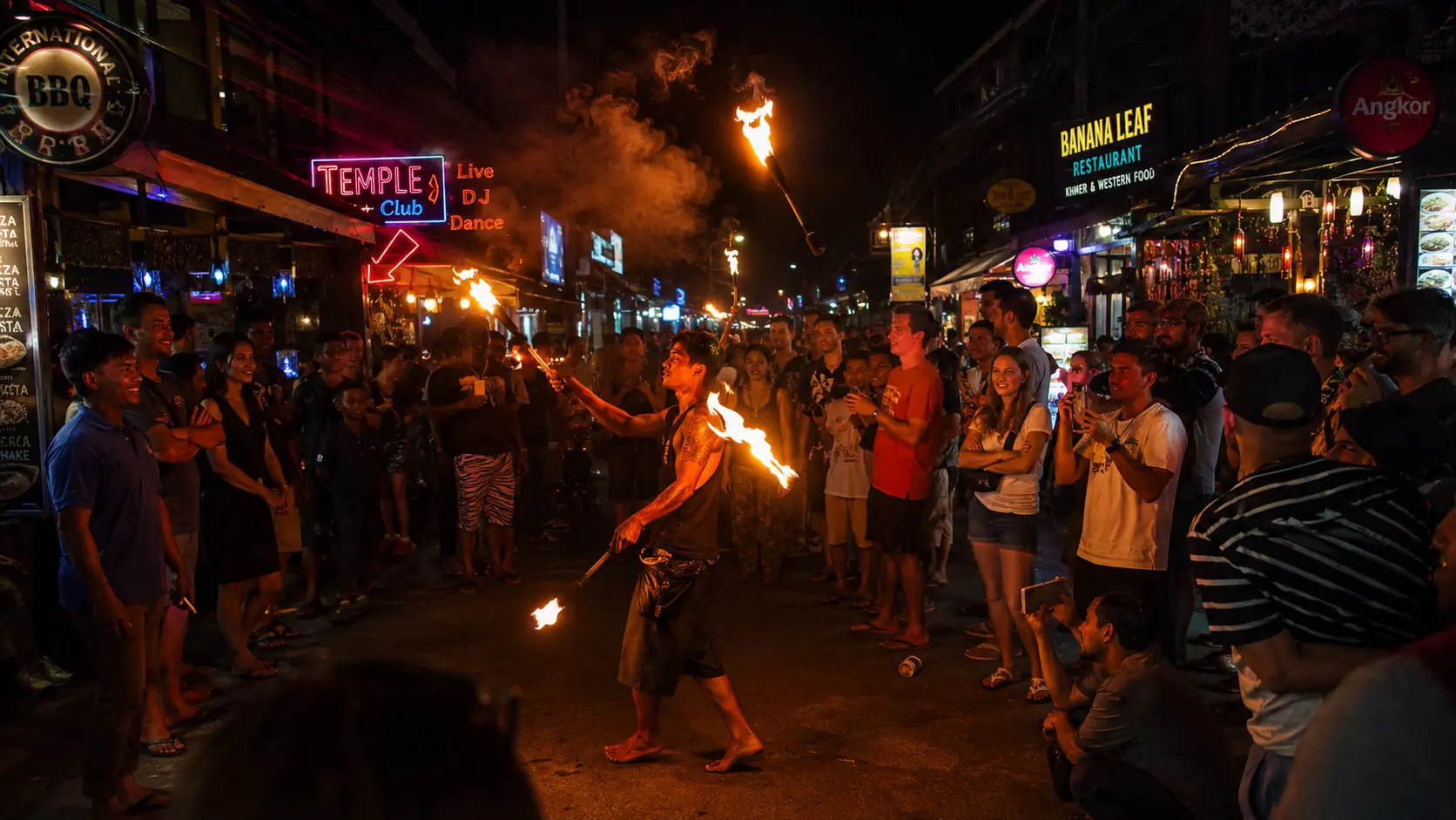 Fire juggler performing on Pub Street in Siem Reap with flames streaking through the night air, a crowd watching against bright neon signs
