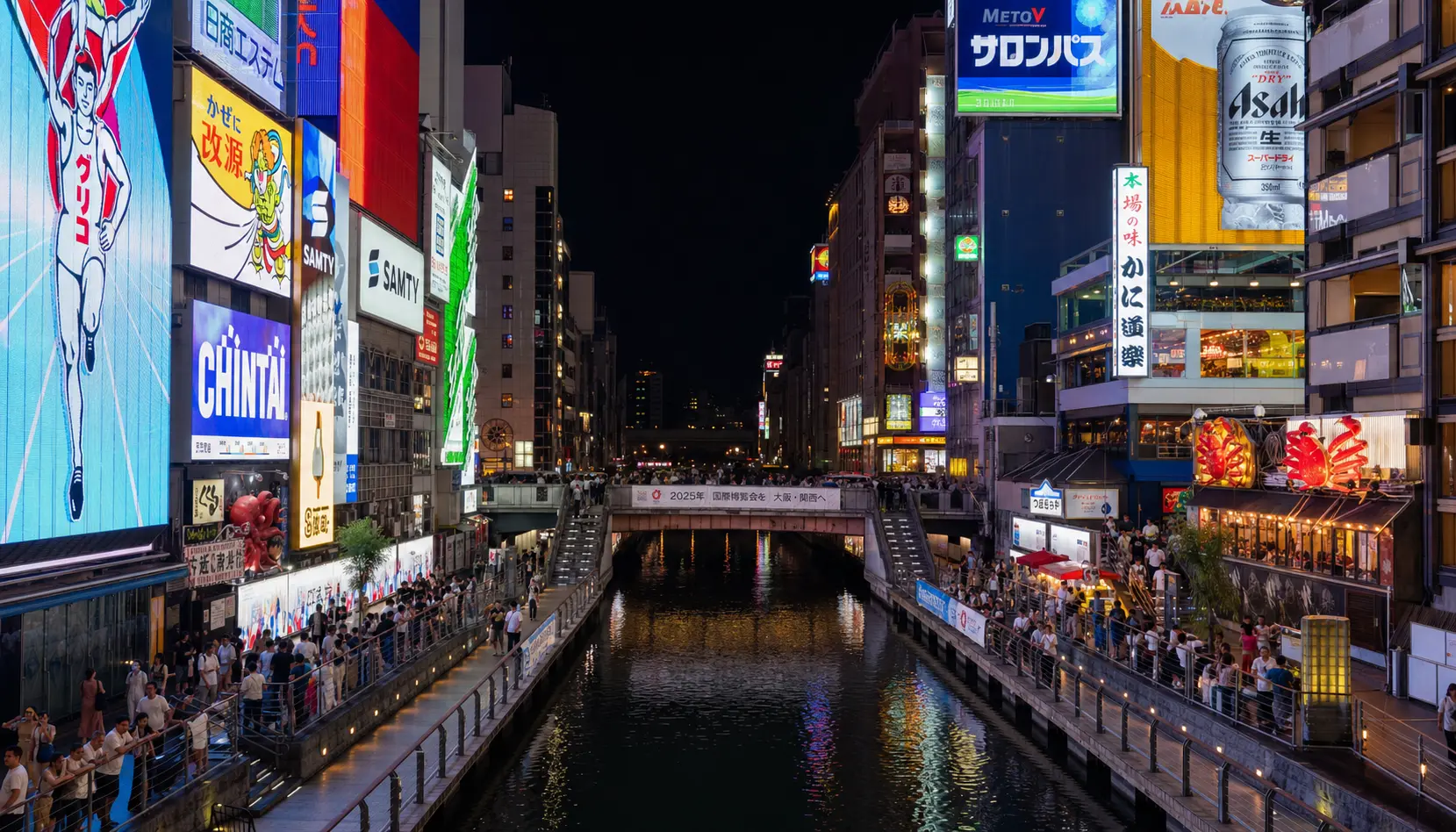 Dotonbori canal in Osaka at night, ablaze with neon billboards and giant illuminated signs reflected in the water, crowds along the walkways.