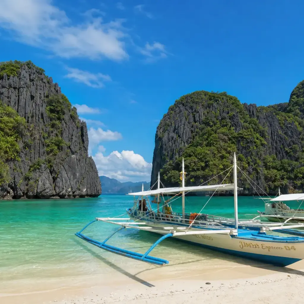 El Nido's limestone cliffs rising from emerald lagoons in Palawan, outrigger bangka boats resting on a white-sand beach
