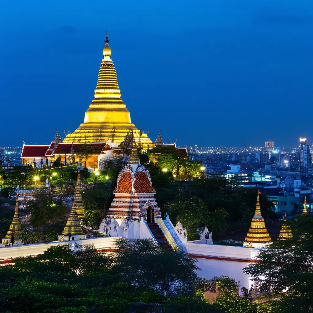 Wat Saket Golden Mount at blue hour, the gleaming gold chedi atop the artificial hill ringed by prayer bells, illuminated city skyline below under a deep cobalt sky