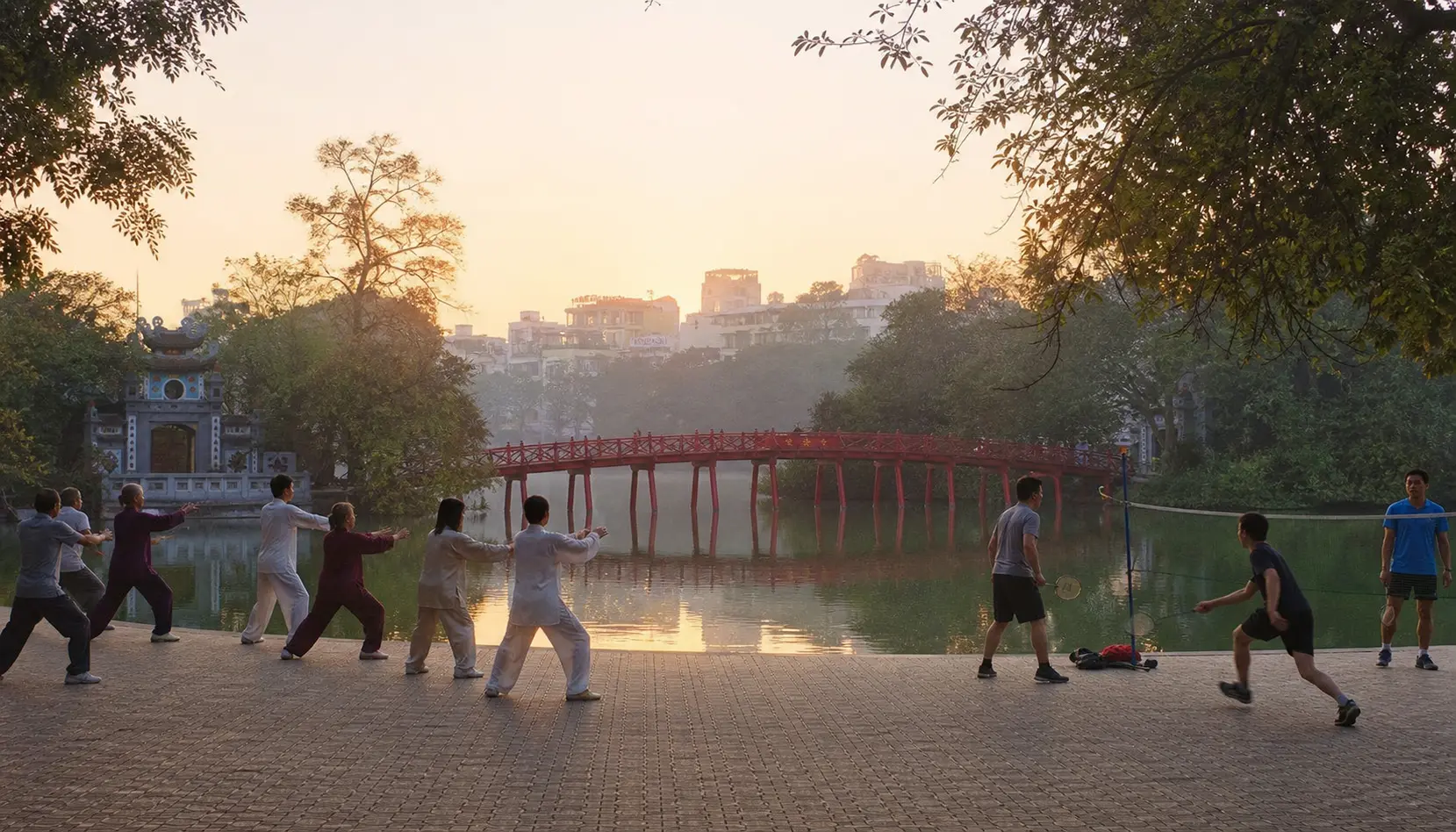 Hoan Kiem Lake in Hanoi at dawn — the red Huc Bridge to Ngoc Son Temple, with locals practising tai chi along the misty lakeside.